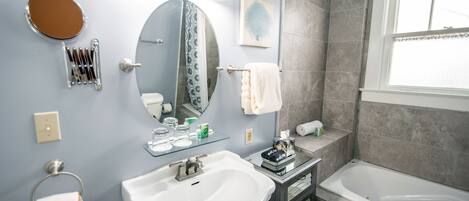 A modern bathroom with a white sink, a round mirror, a glass shower enclosure, and a bathtub.