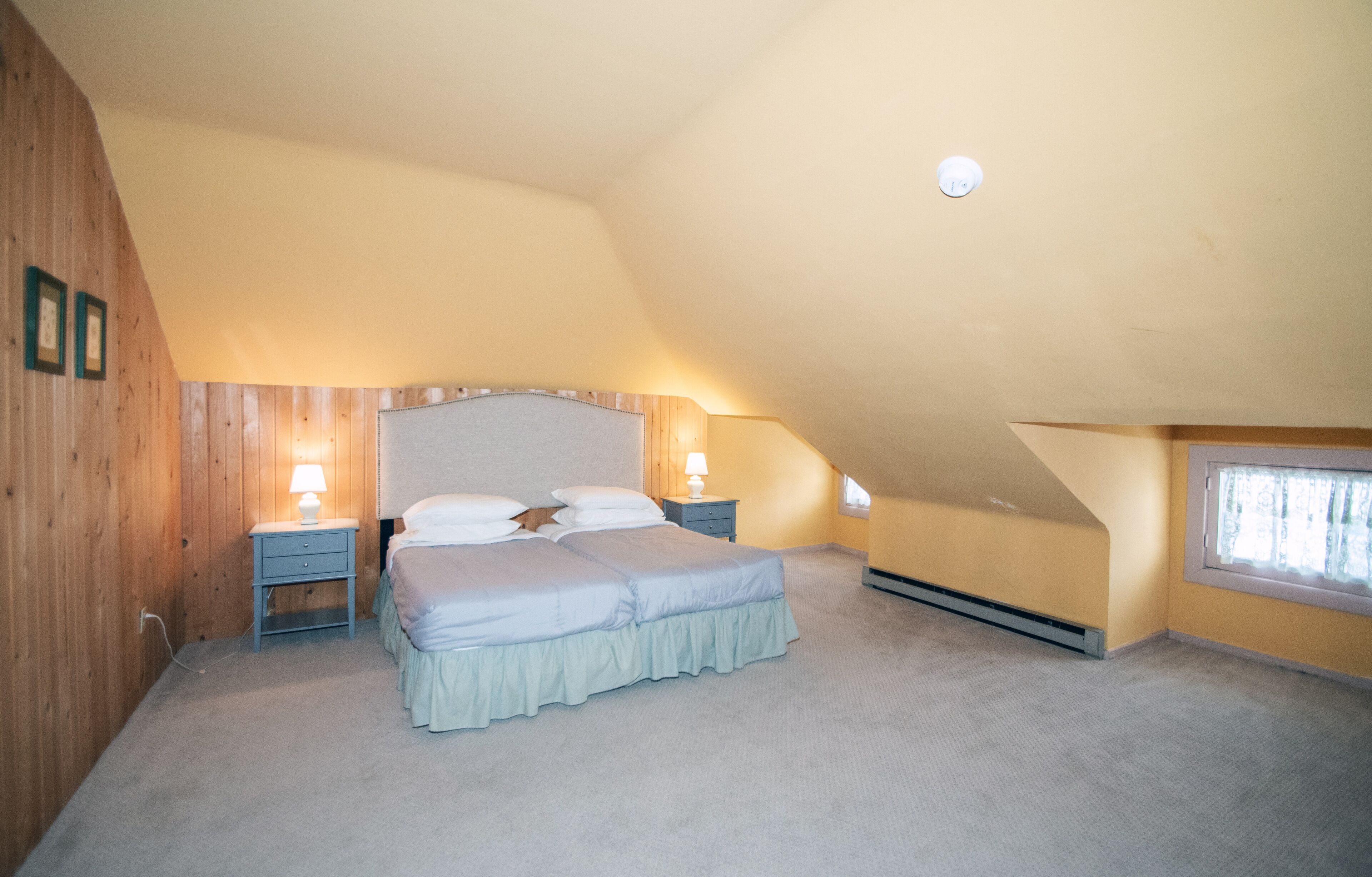 A bedroom with a sloped ceiling, a bed with a headboard, two bedside tables with lamps, and a window.