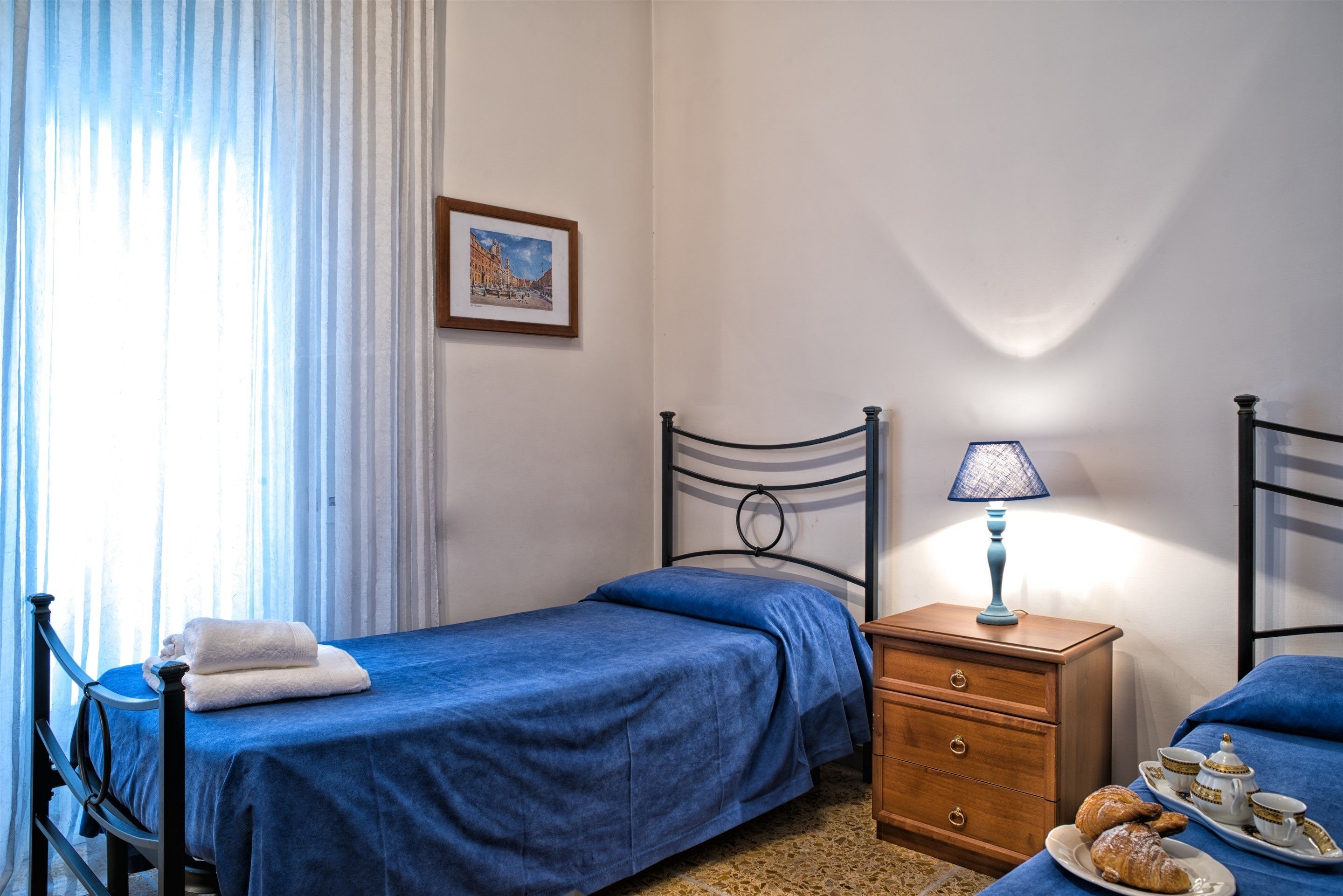 A bedroom with two single beds, a wooden nightstand with a lamp, and a breakfast tray with croissants.