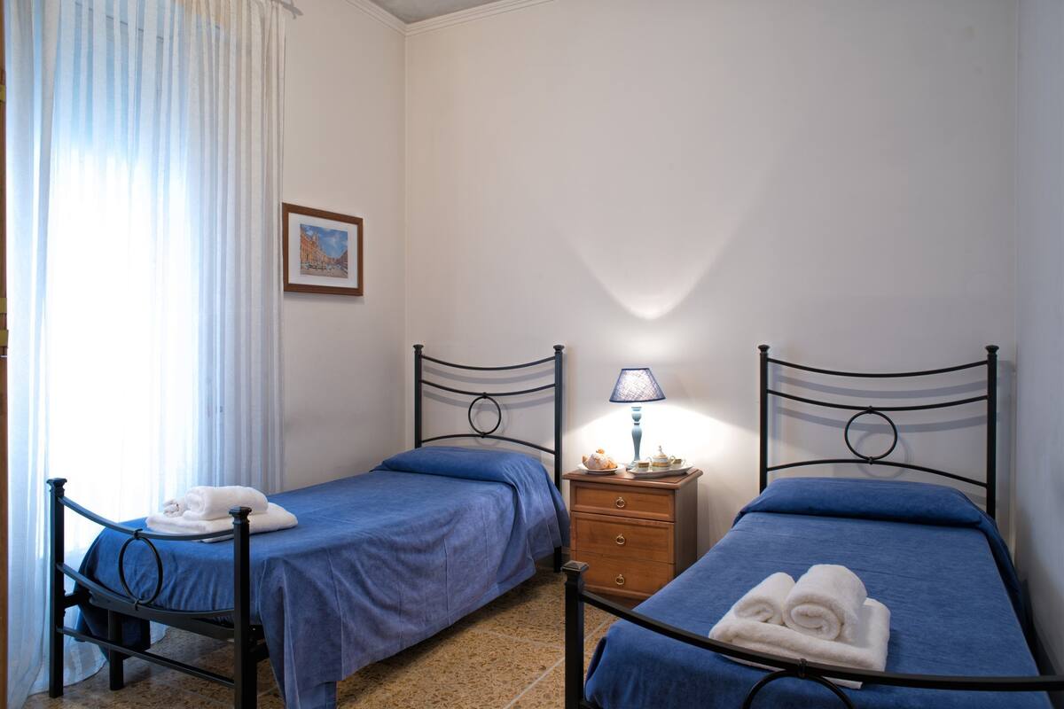 A room with two single beds, a nightstand with a lamp, and a framed picture on the wall.