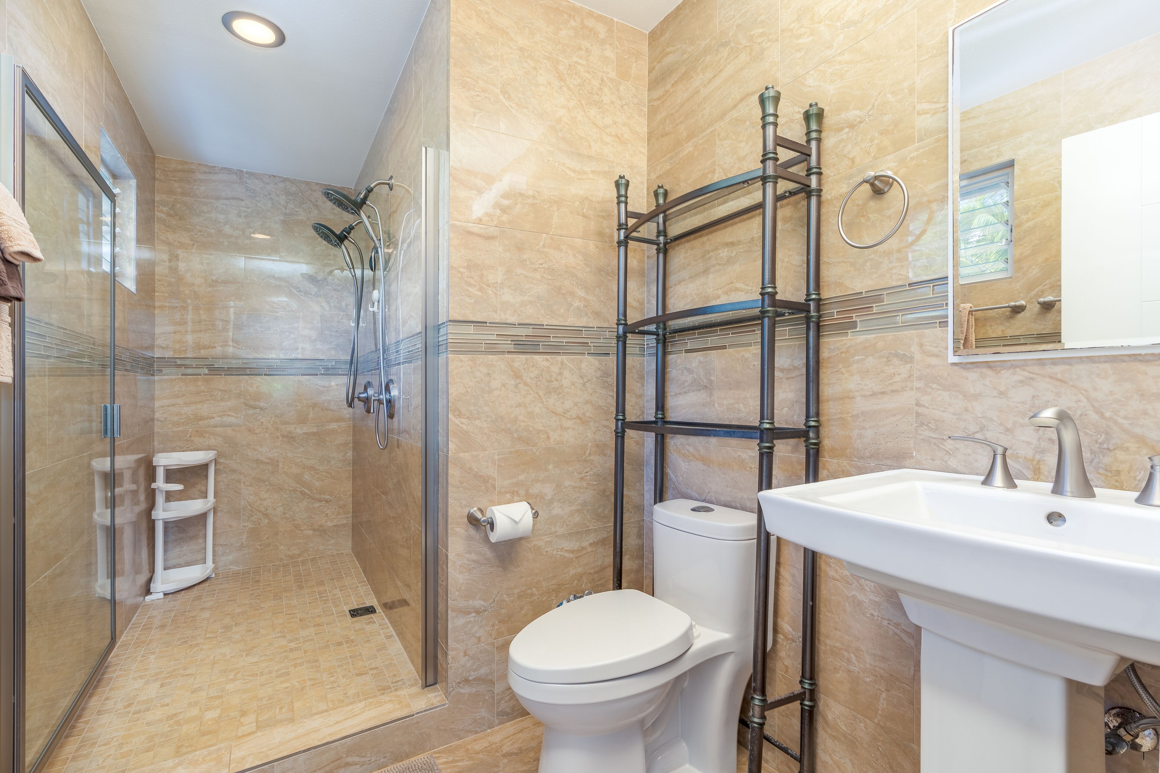 Un baño con ducha de vidrio, inodoro blanco y lavamanos con espejo.