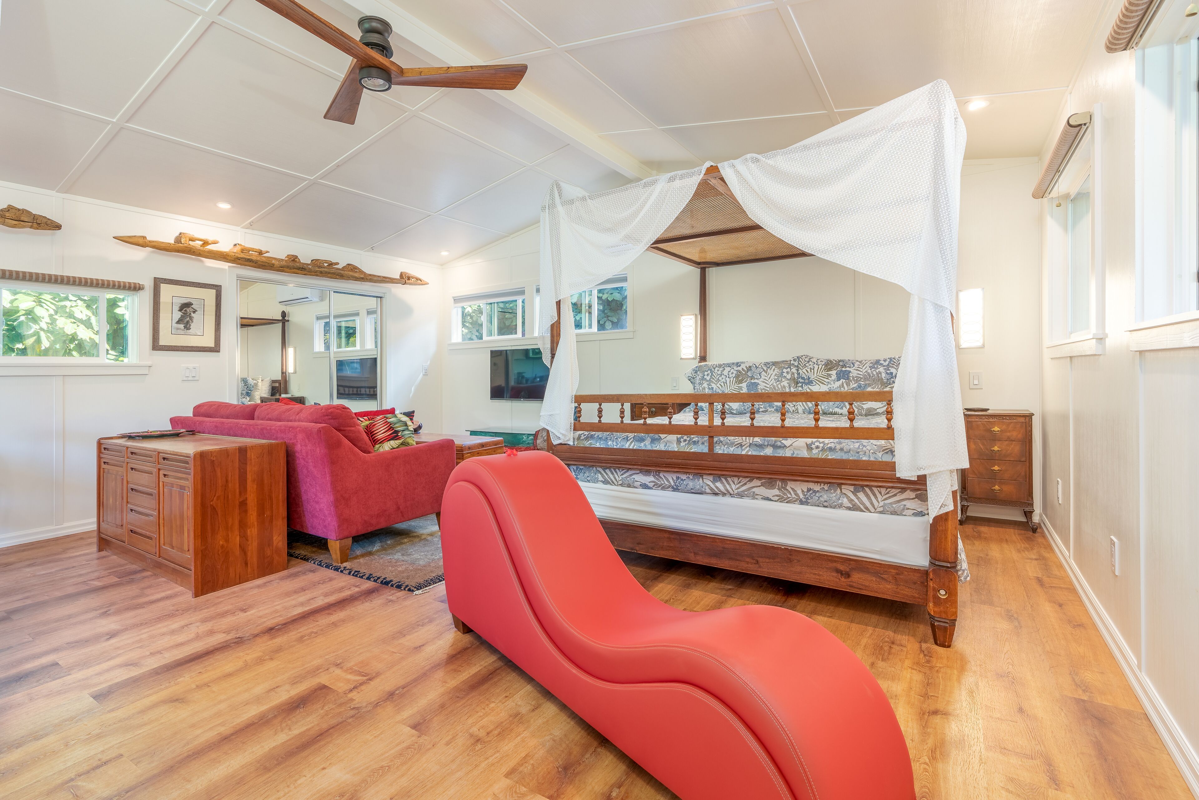 Une chambre à coucher avec un lit à baldaquin, un fauteuil rouge, une commode en bois et un ventilateur de plafond.