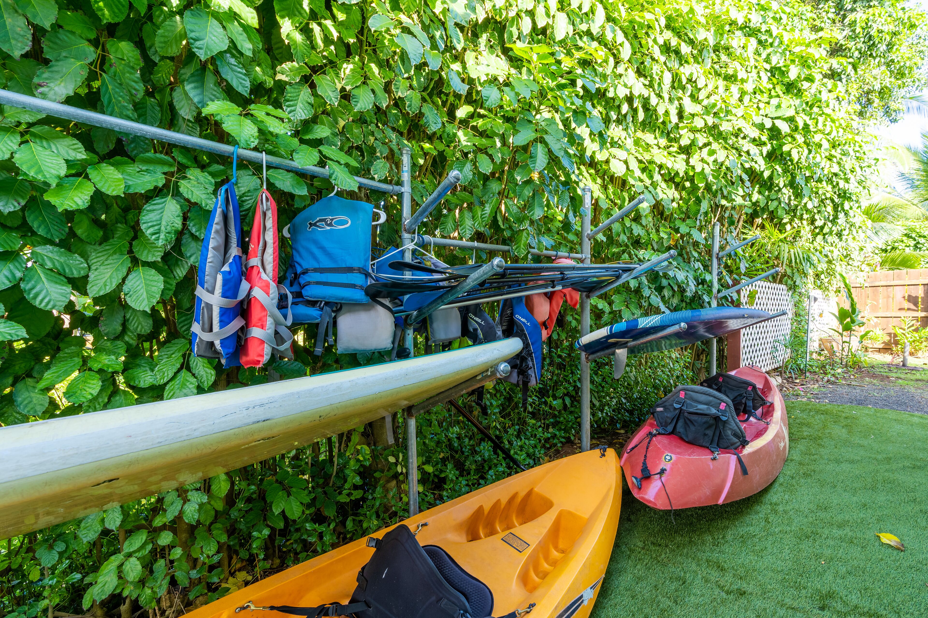 Un kayak y una canoa atados a un estante metálico, con un kayak rojo en el suelo y un kayak azul en el estante.