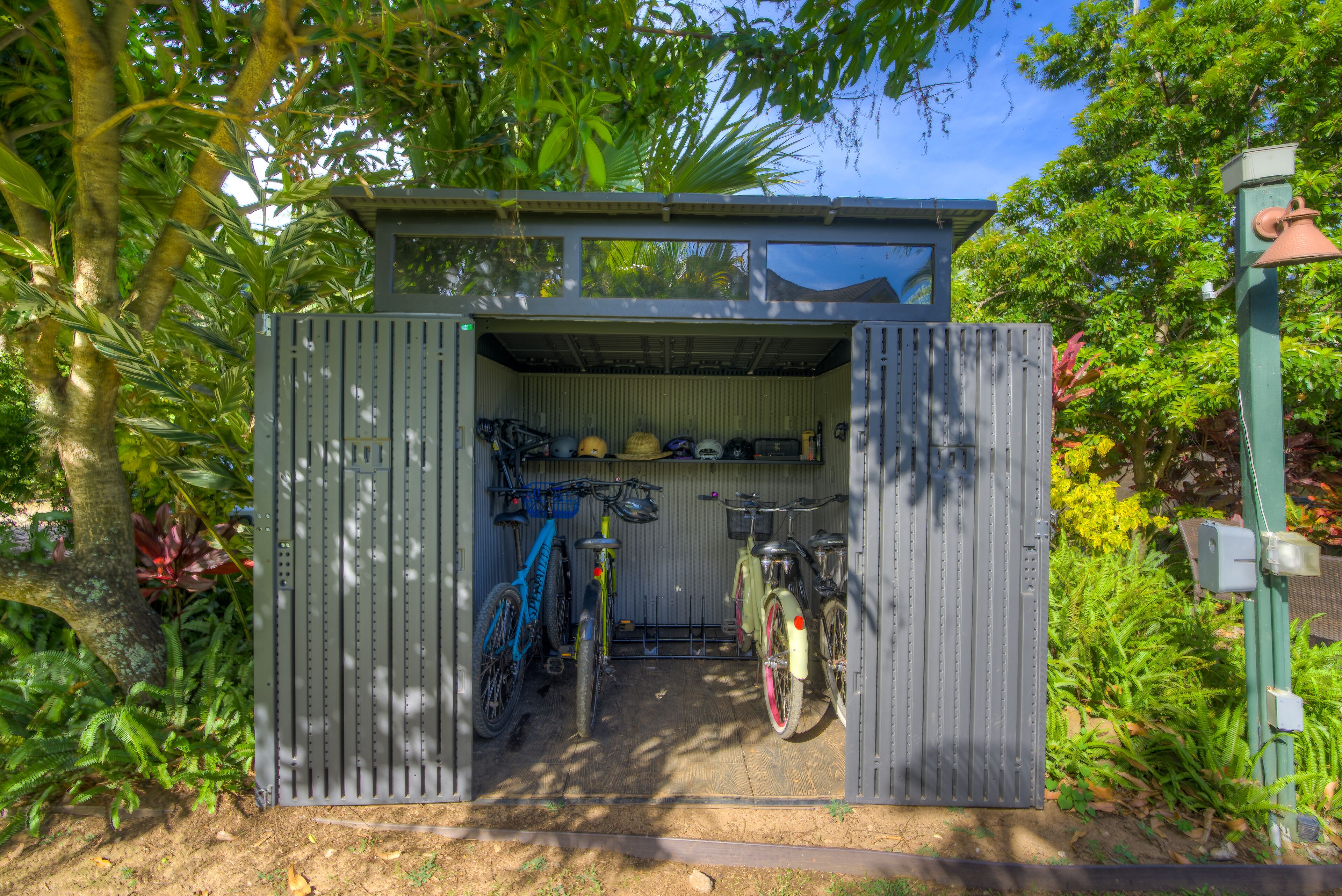A small, enclosed bicycle storage area with a roof, surrounded by lush greenery.