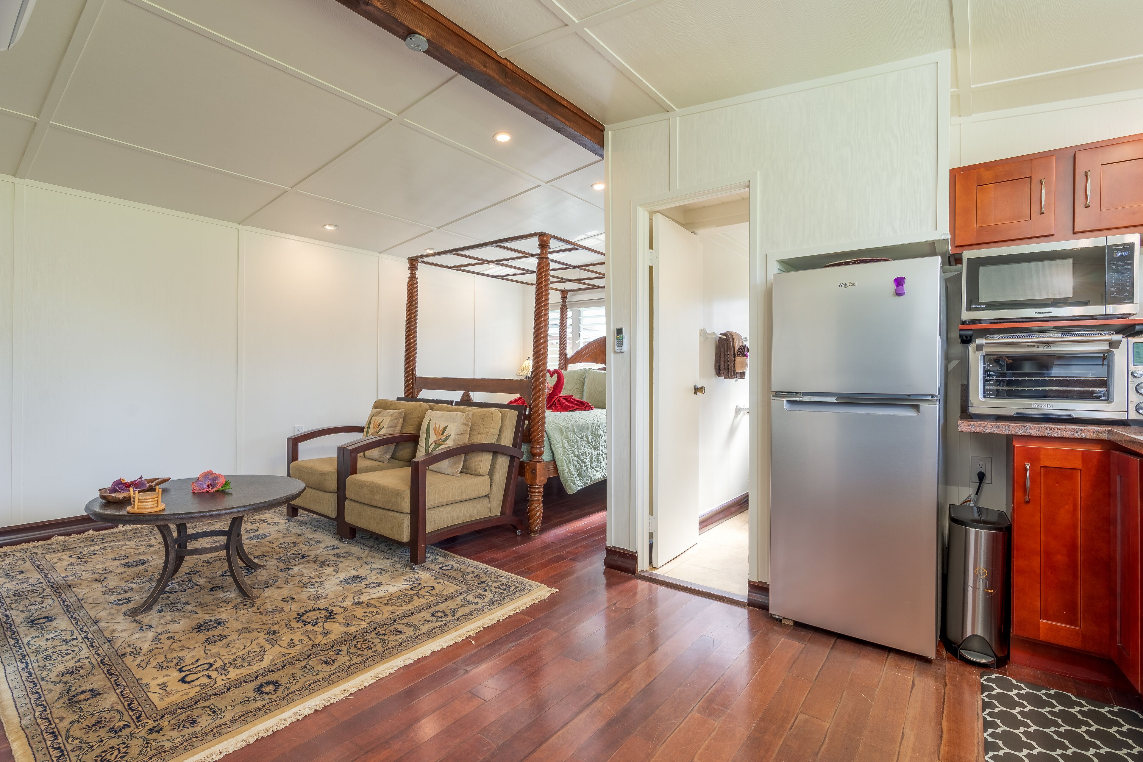 Une chambre dotée d’un lit à baldaquin, d’une table à manger, d’un coin cuisine avec un réfrigérateur et un four à micro-ondes, et d’un tapis à motifs.