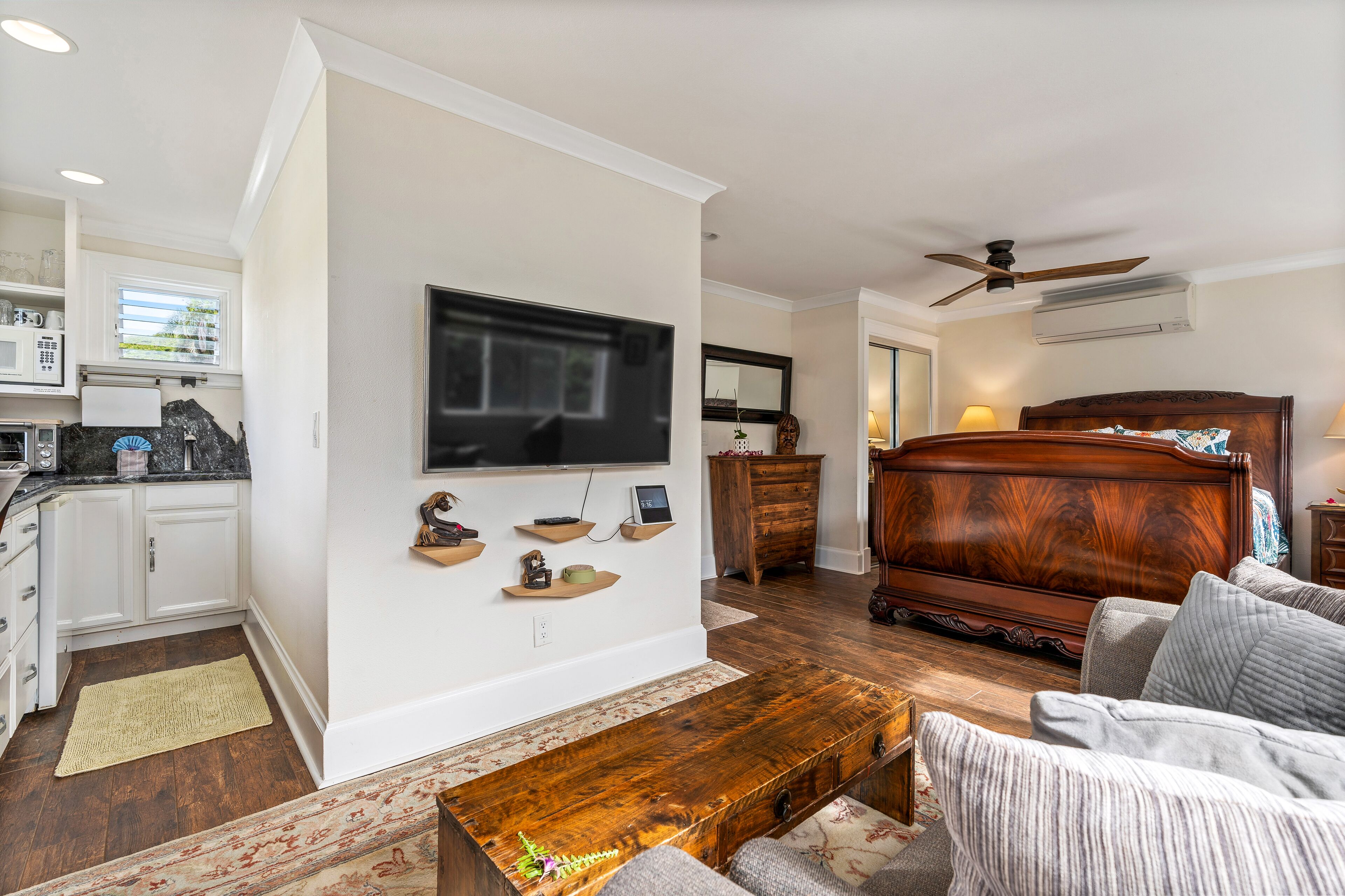 Una sala moderna con una mesa de centro de madera, un sofá, un televisor montado en la pared y una cama grande con cabecera de madera.