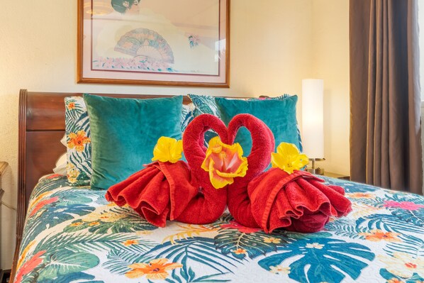 A bed with floral bedding, two pillows, and a heart-shaped towel arrangement. - Fern Grotto Inn (Kapaa)