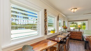 A spacious room with large windows, a wooden dining table, and a cozy seating area. - Fern Grotto Inn (Kapaa)