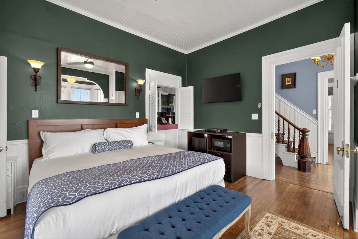 Une chambre à coucher avec un grand lit, une commode, un miroir, une télévision et un escalier.