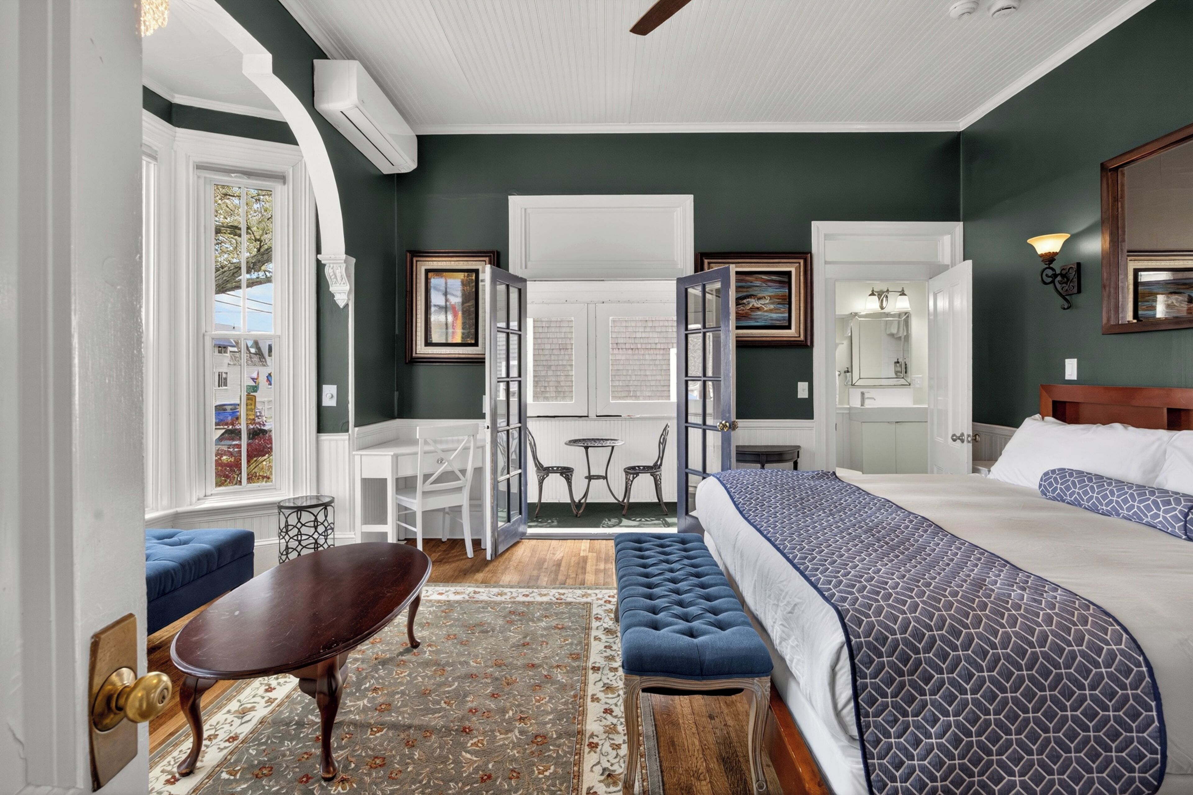 A bedroom with a large bed, a sitting area with a table and chairs, and a view through a door to a dining area.