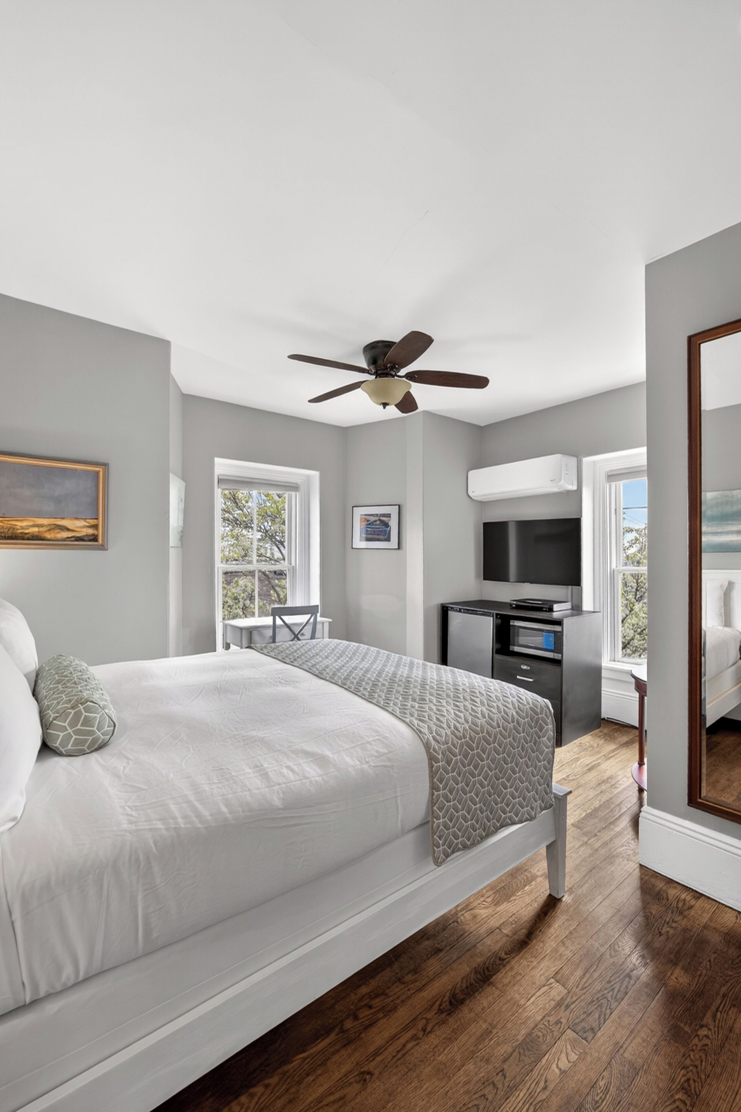 A bedroom with a bed, a desk, a television, and a ceiling fan.