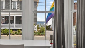 Uitzicht door een raam, met een witte tafel op de voorgrond, een huis met veranda en een vlag.