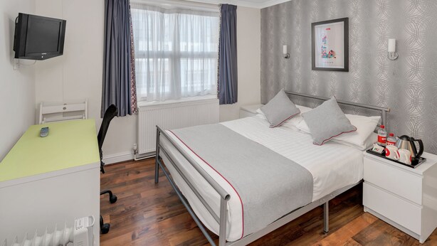 A neatly arranged bedroom with a bed, bedside table, and a desk with a chair. - Flexistay Tulsi Aparthotel (Croydon)
