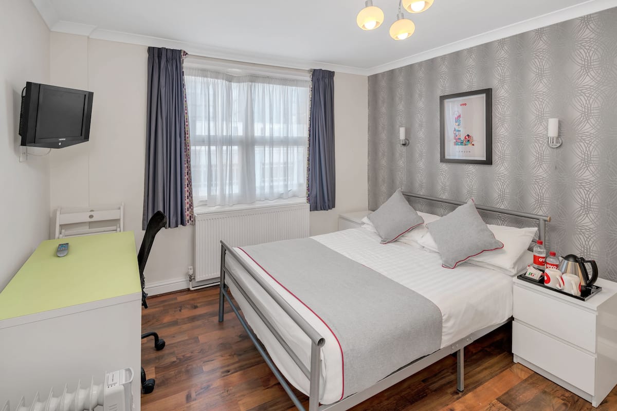 Ein ordentlich eingerichtetes Schlafzimmer mit Bett, Nachttisch und Schreibtisch mit Stuhl.