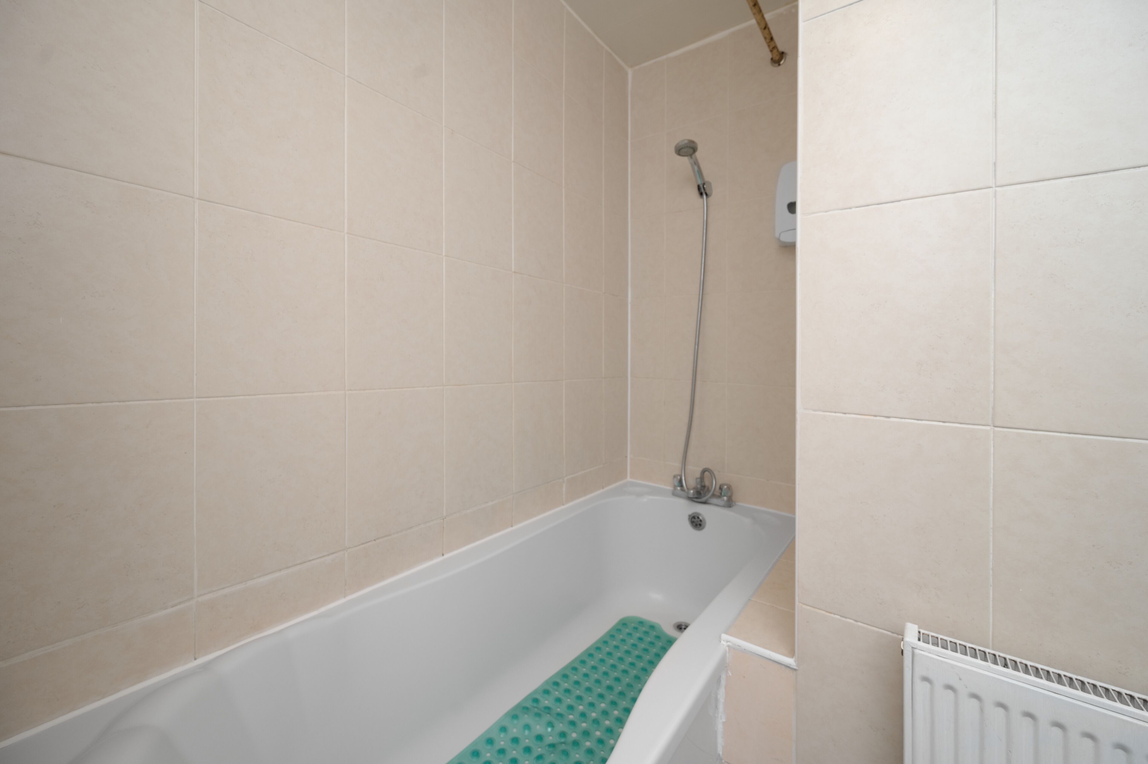 Un bagno con vasca, doccia e termosifone bianco.