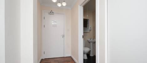 A hallway with wooden flooring, a white door, and a bathroom with a sink and toilet.