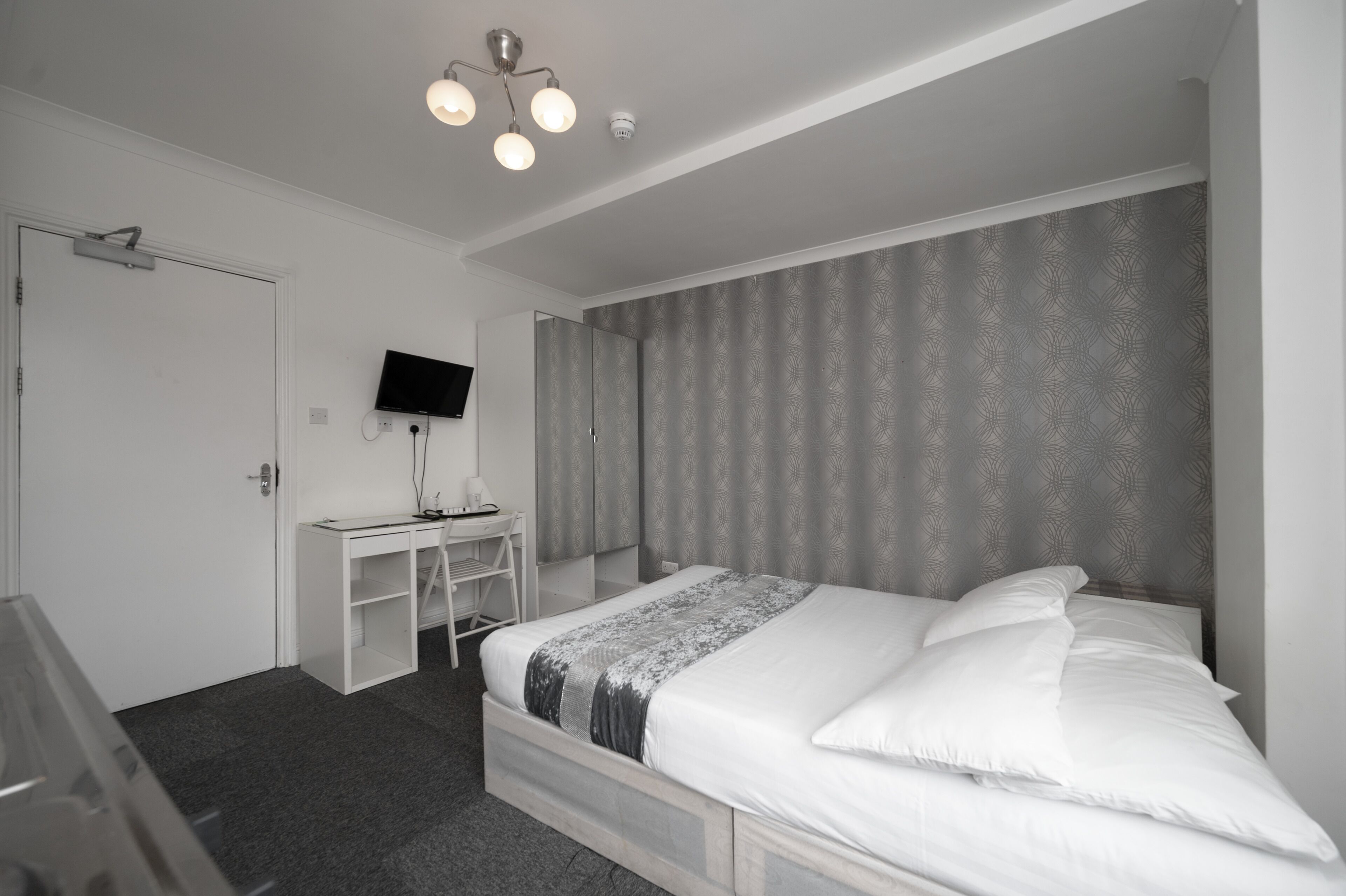 A bedroom with a bed, a desk, a television, and a door.