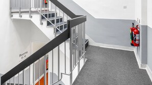 A modern staircase with a grey carpet, white walls, and a fire extinguisher on the wall. - Flexistay Tulsi Aparthotel (Croydon)