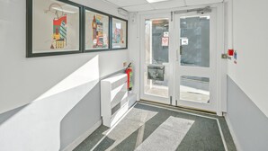 A hallway with framed artwork, a fire extinguisher, and a door with a glass panel. - Flexistay Tulsi Aparthotel (Croydon)