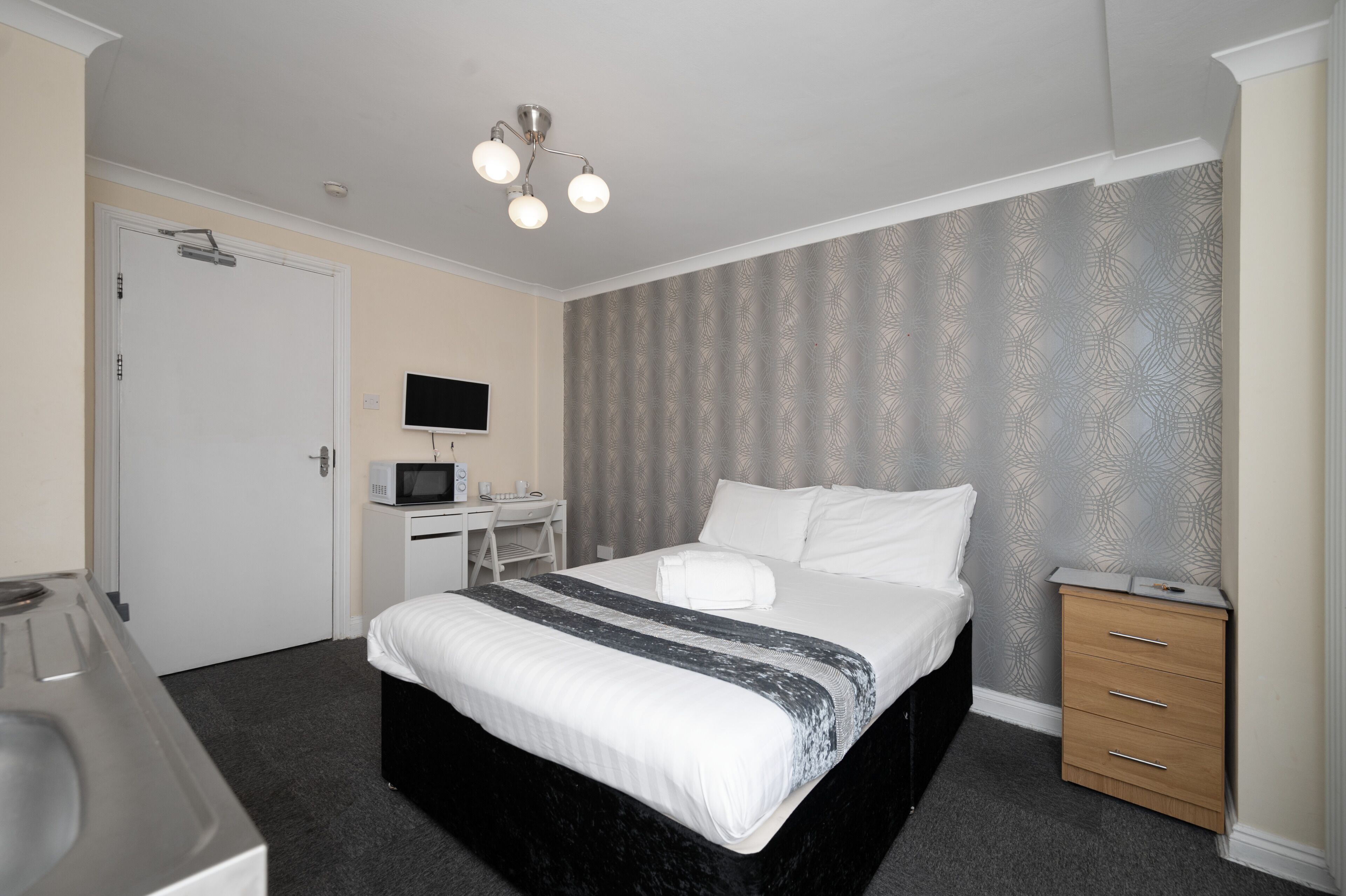 Une chambre d’hôtel équipée d’un lit, d’un bureau avec un ordinateur, d’un micro-ondes et d’un téléviseur fixé au mur.