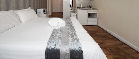 Een hotelkamer met een groot bed, een kleine kitchenette en een badkamer op de achtergrond.