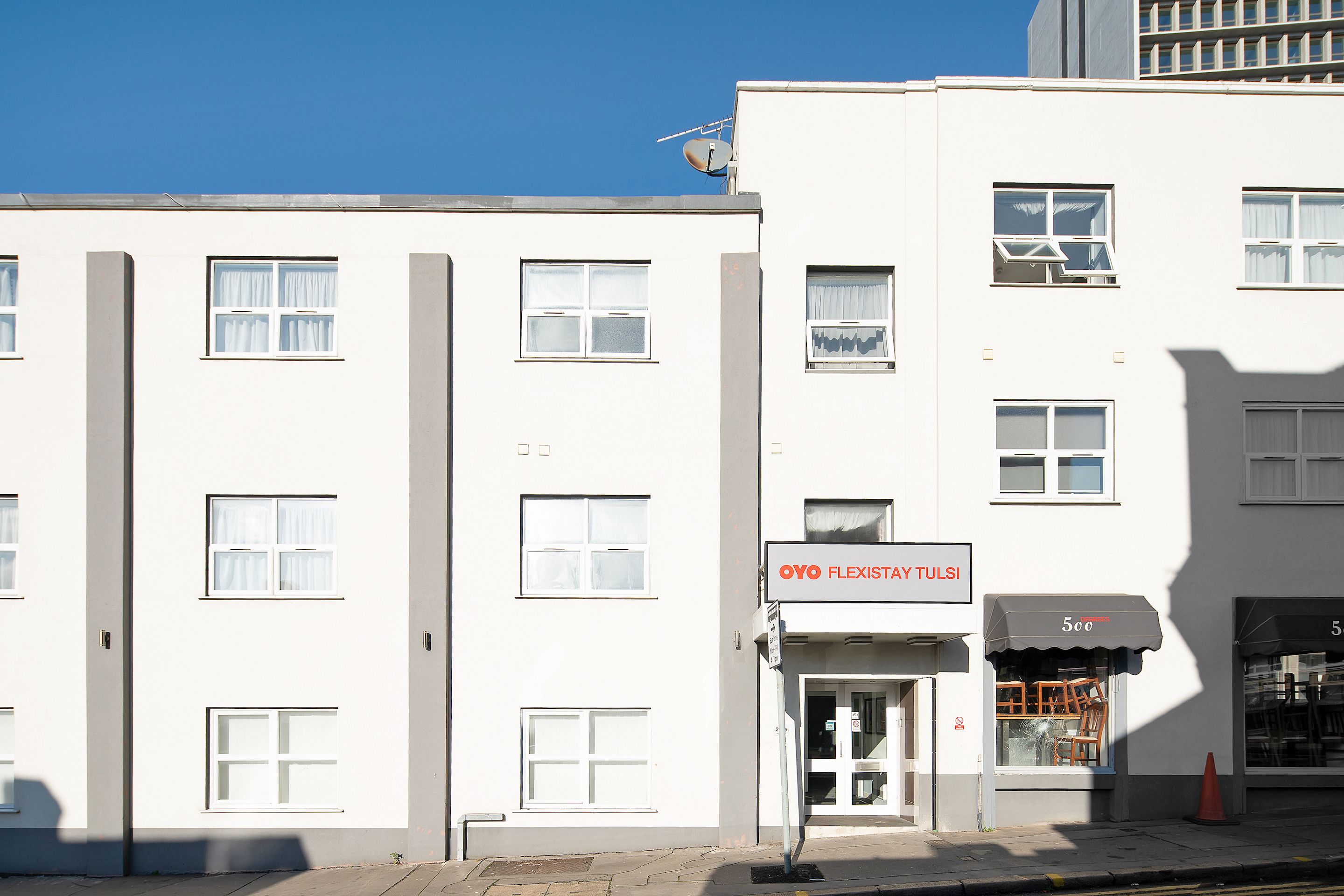Un edificio blanco con múltiples ventanas y un cartel que dice 'OYO FLEXISTAY TULSI'.