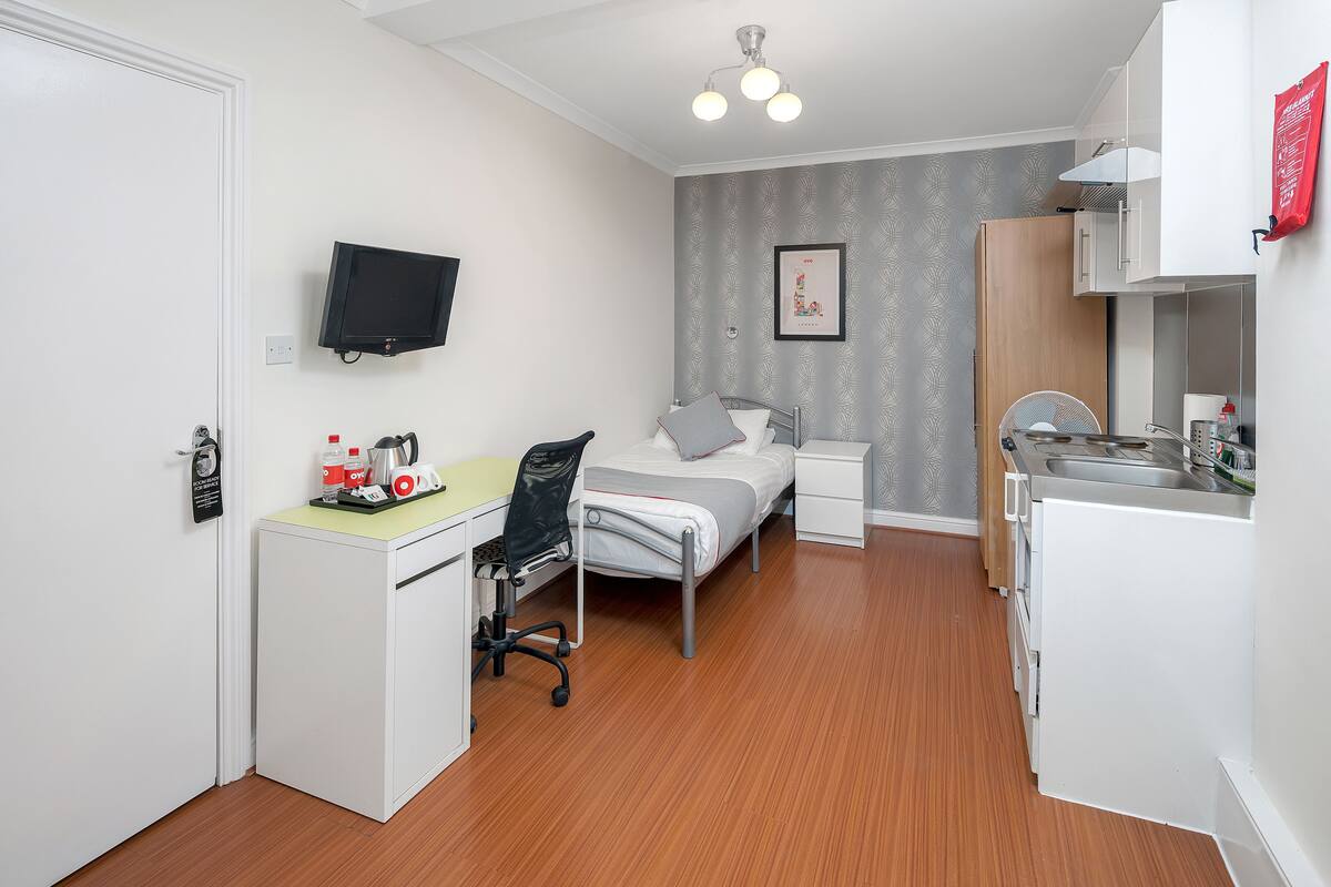 Ein kleines Hotelzimmer mit Bett, Nachttisch, Schreibtisch, Stuhl und einer kleinen Küchenzeile.