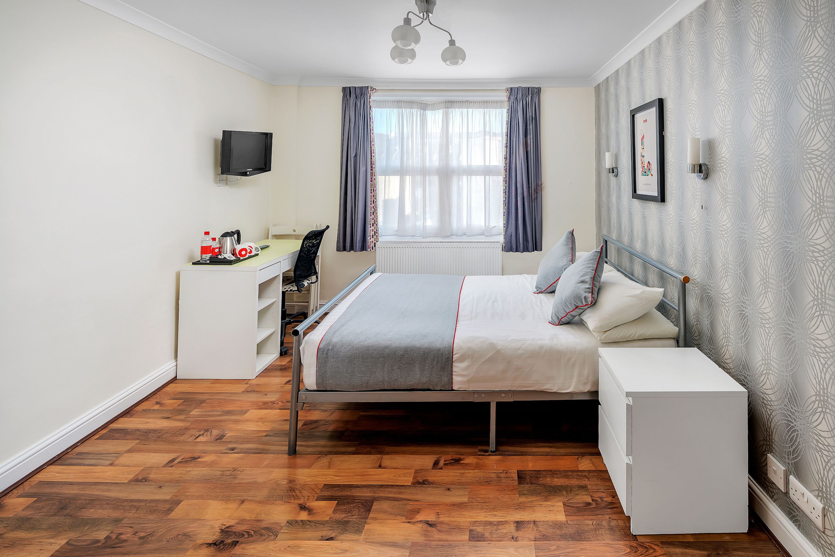Un dormitorio con cama, mesita de noche, escritorio, silla y televisor montado en la pared.