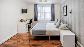 Un dormitorio con cama, mesita de noche, escritorio, silla y televisor montado en la pared.