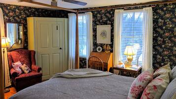 Quarto com cama, cadeira, escrivaninha, ventilador de teto e papel de parede floral.