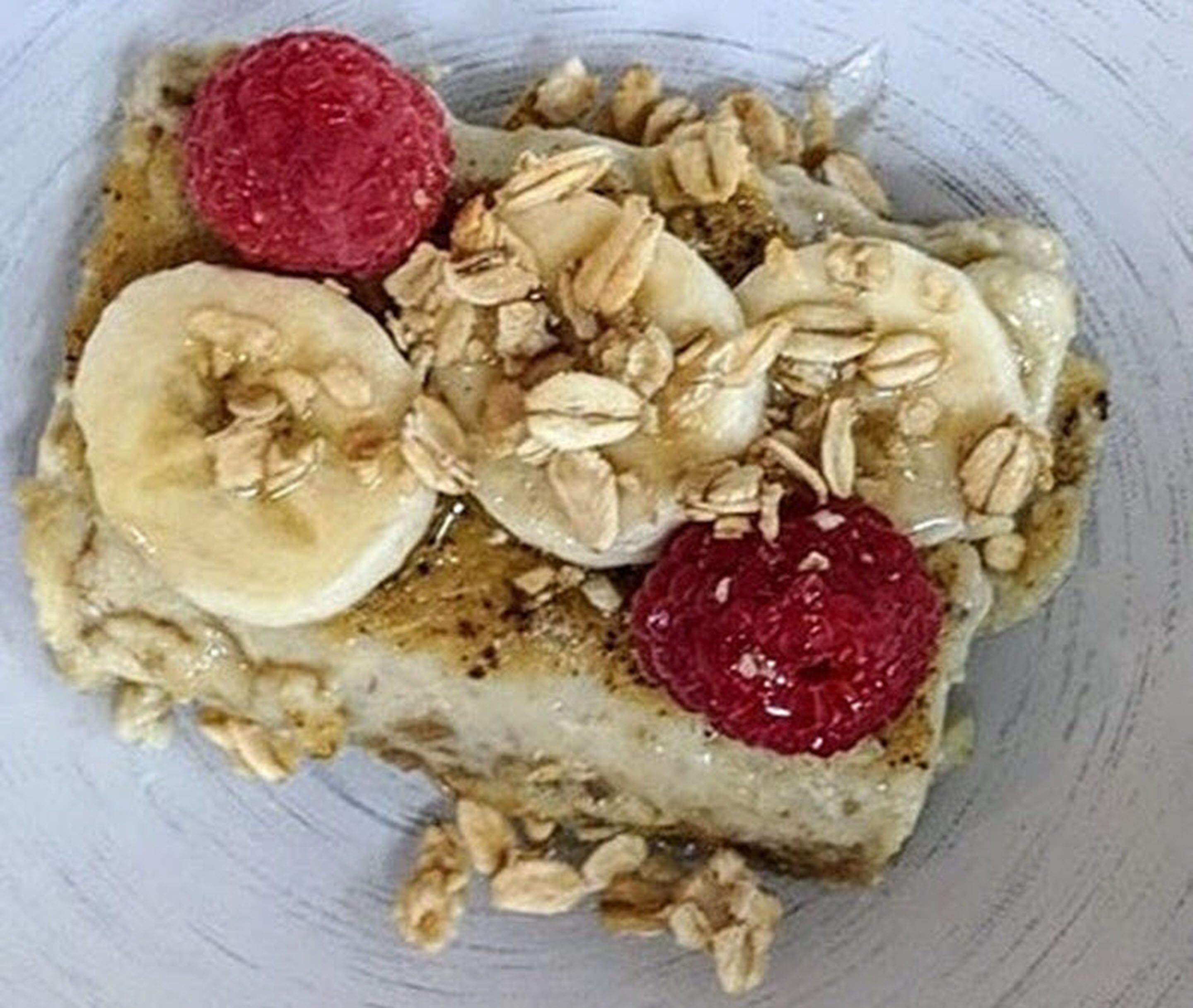 A plate with oatmeal topped with banana slices, raspberries, and walnuts.