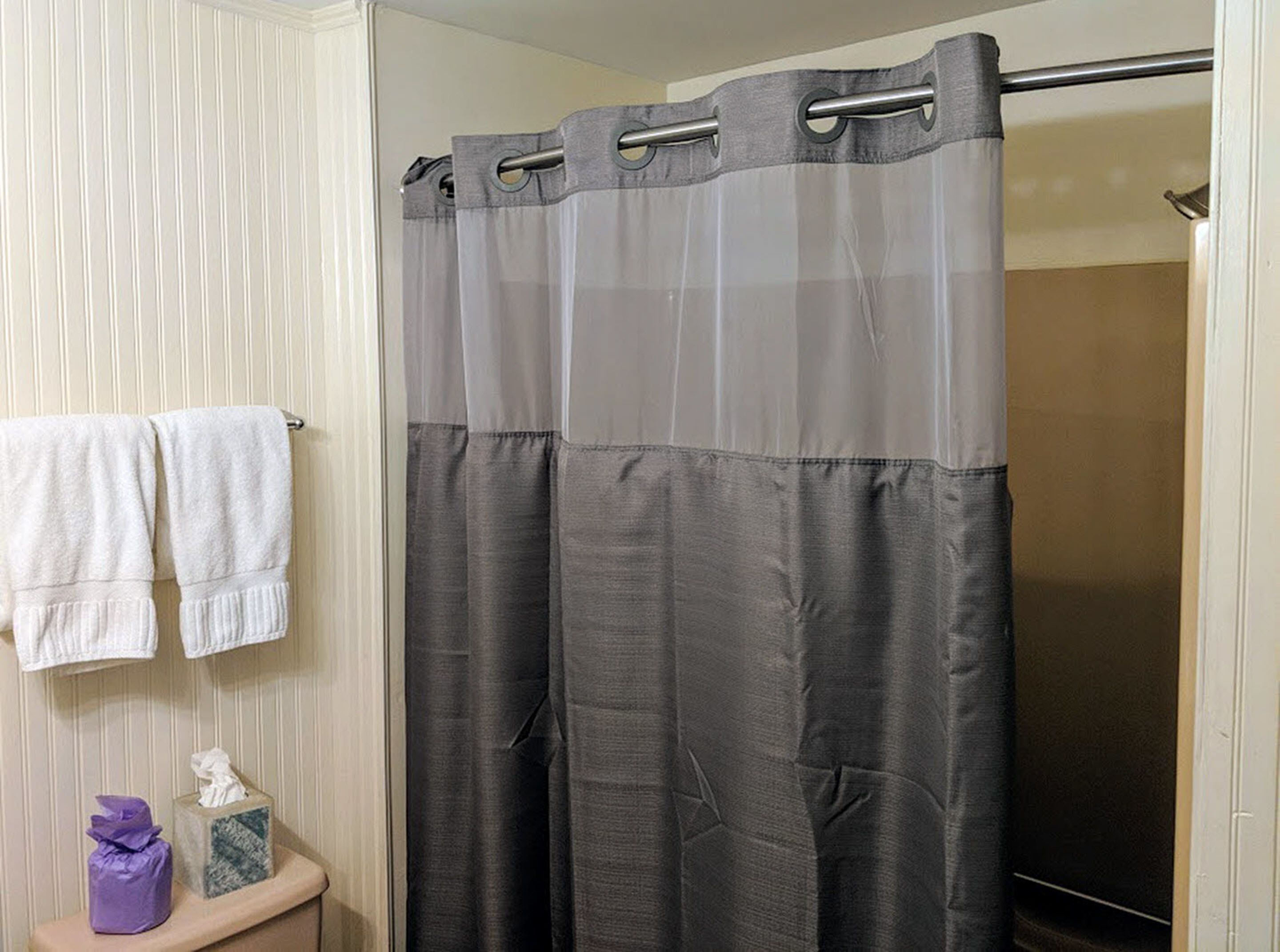 A bathroom with a shower curtain, towels, and a tissue box on a shelf.