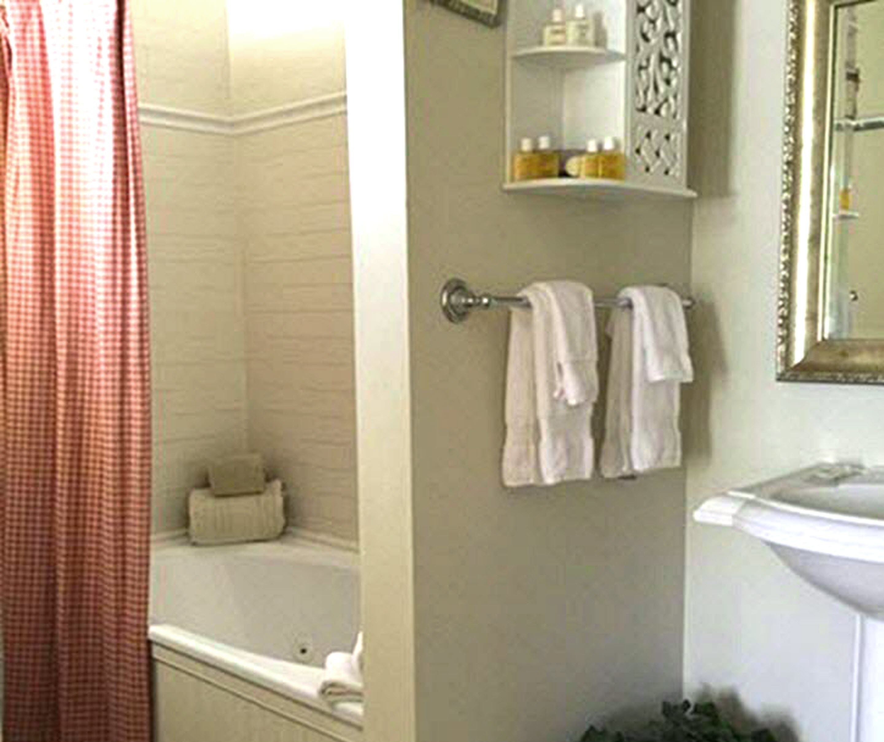 Une salle de bain avec une baignoire, un porte-serviettes avec deux serviettes, une étagère avec des articles de toilette et un miroir.
