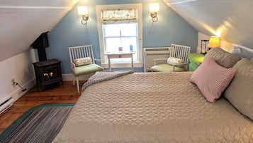 Ein gemütliches Schlafzimmer im Dachgeschoss mit einem großen Bett, zwei Sesseln, einem kleinen Tisch, einem Heizkörper und einem Kamin.