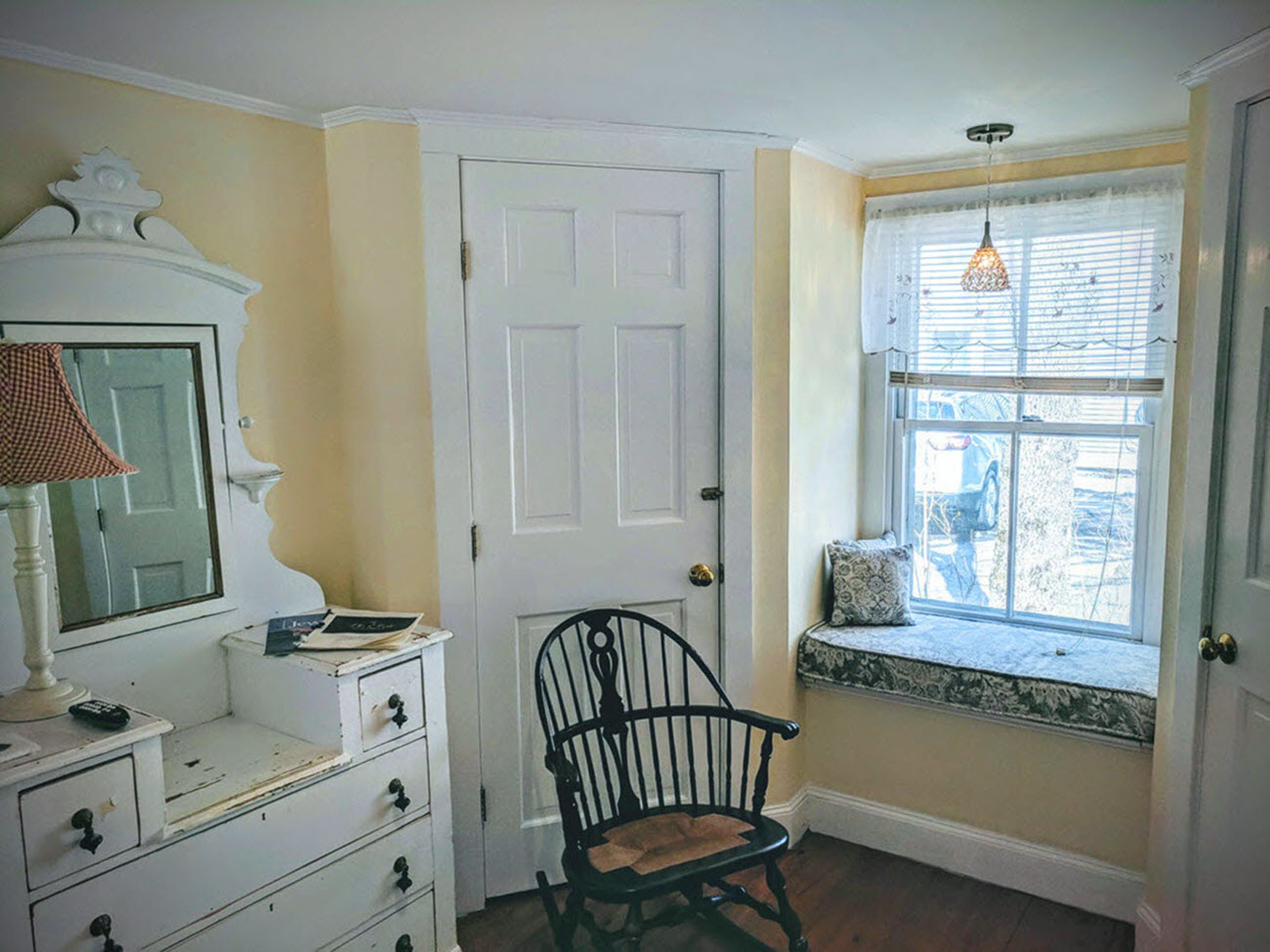 A room with a white dresser, a chair, a window with a view, and a door.