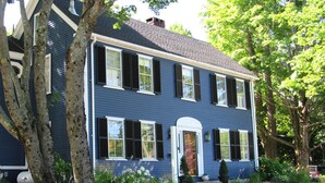 A two-story house with a symmetrical facade, a central entrance with a white door, and a small front yard with a lawn and a few trees. - Elms of Camden (Camden)