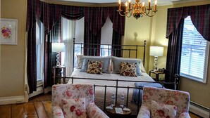 A bedroom with a four-poster bed, two armchairs, a chandelier, and plaid curtains. - Elms of Camden (Camden)