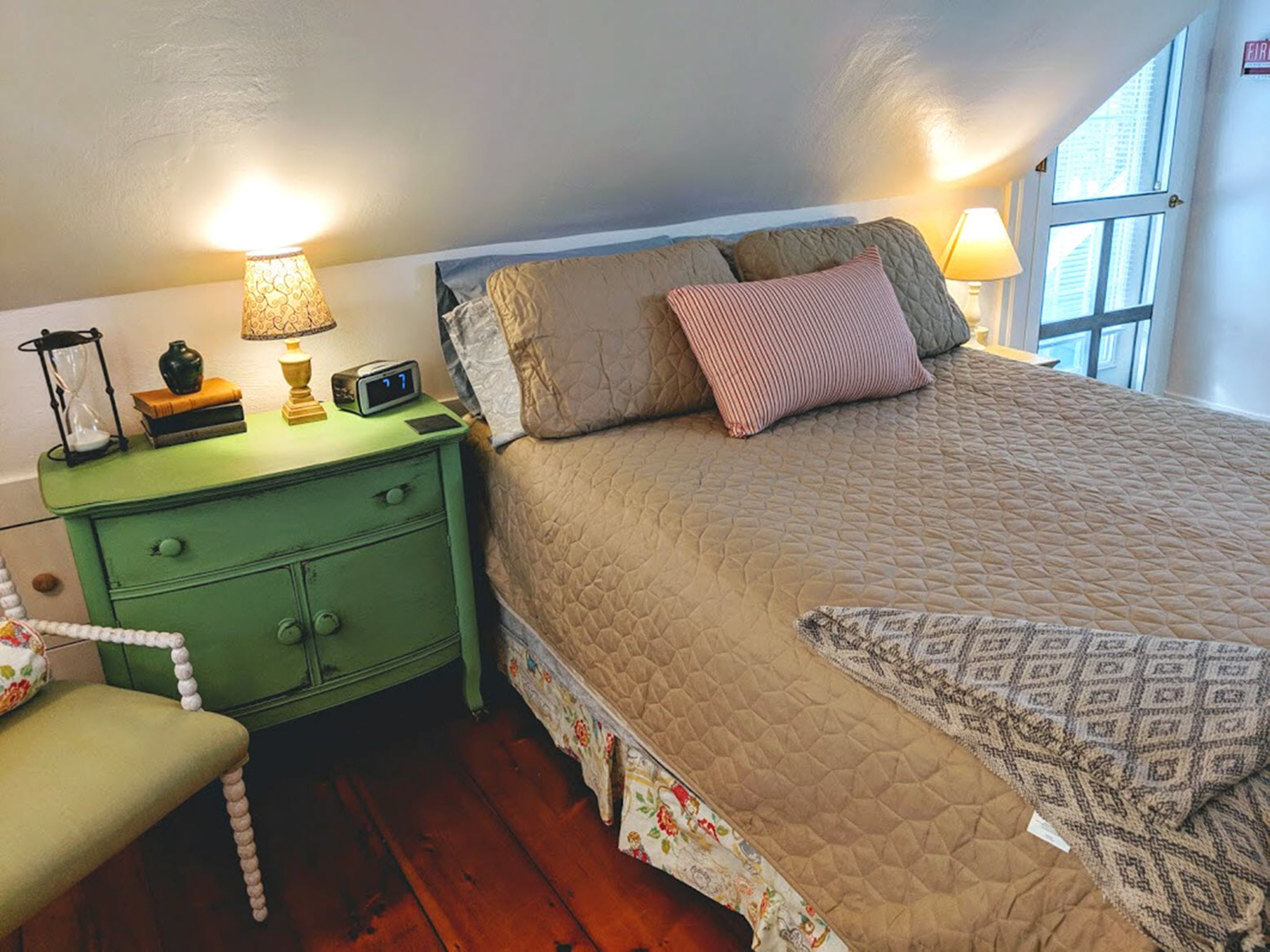 A bedroom with a bed, a nightstand, a lamp, a chair, and a window.