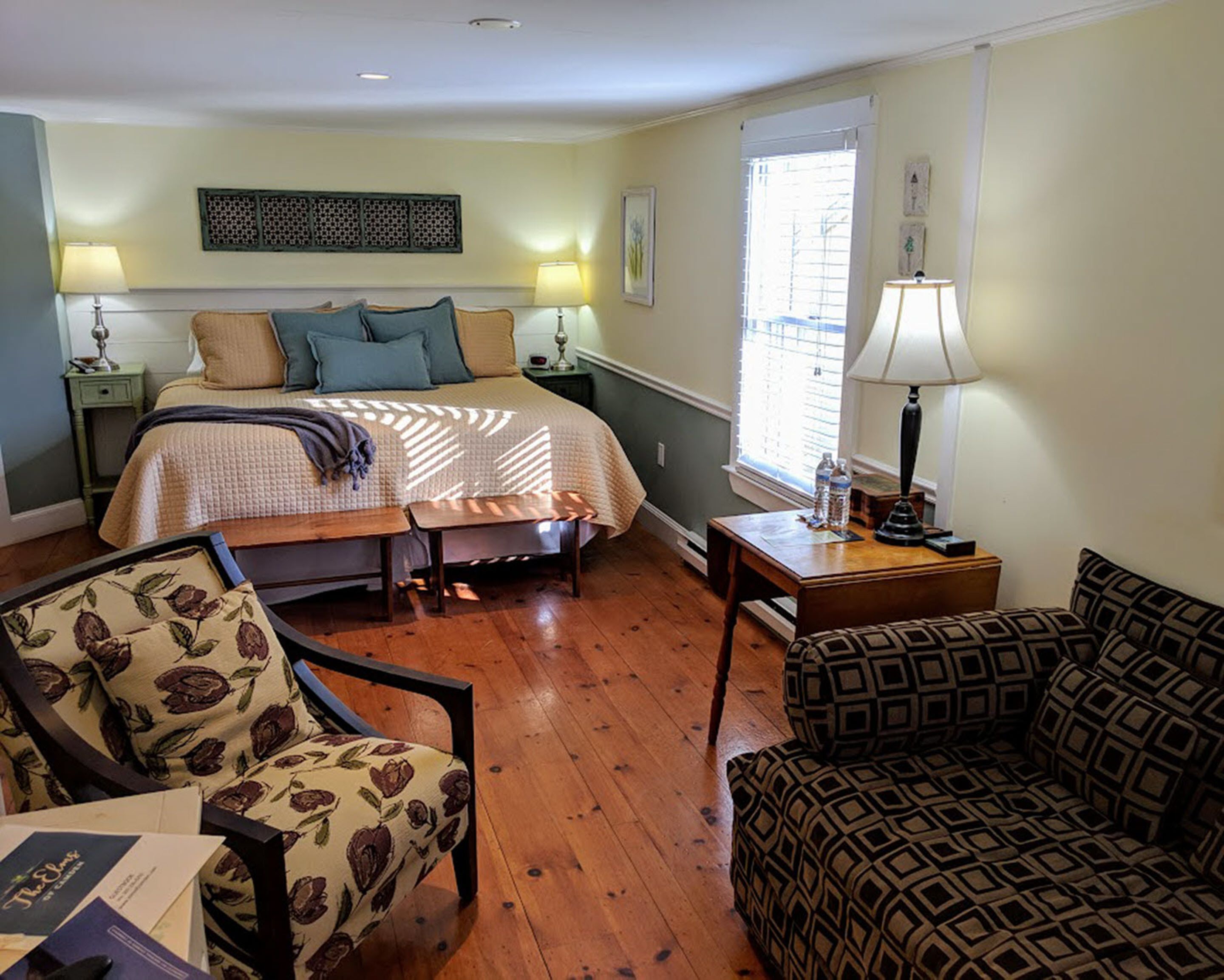 A cozy bedroom with a bed, bedside tables, a chair, a sofa, and a window with blinds.