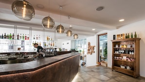 A modern bar area with a long counter, hanging pendant lights, and a variety of bottles and glasses on shelves. - Hotel Troja (Prague)
