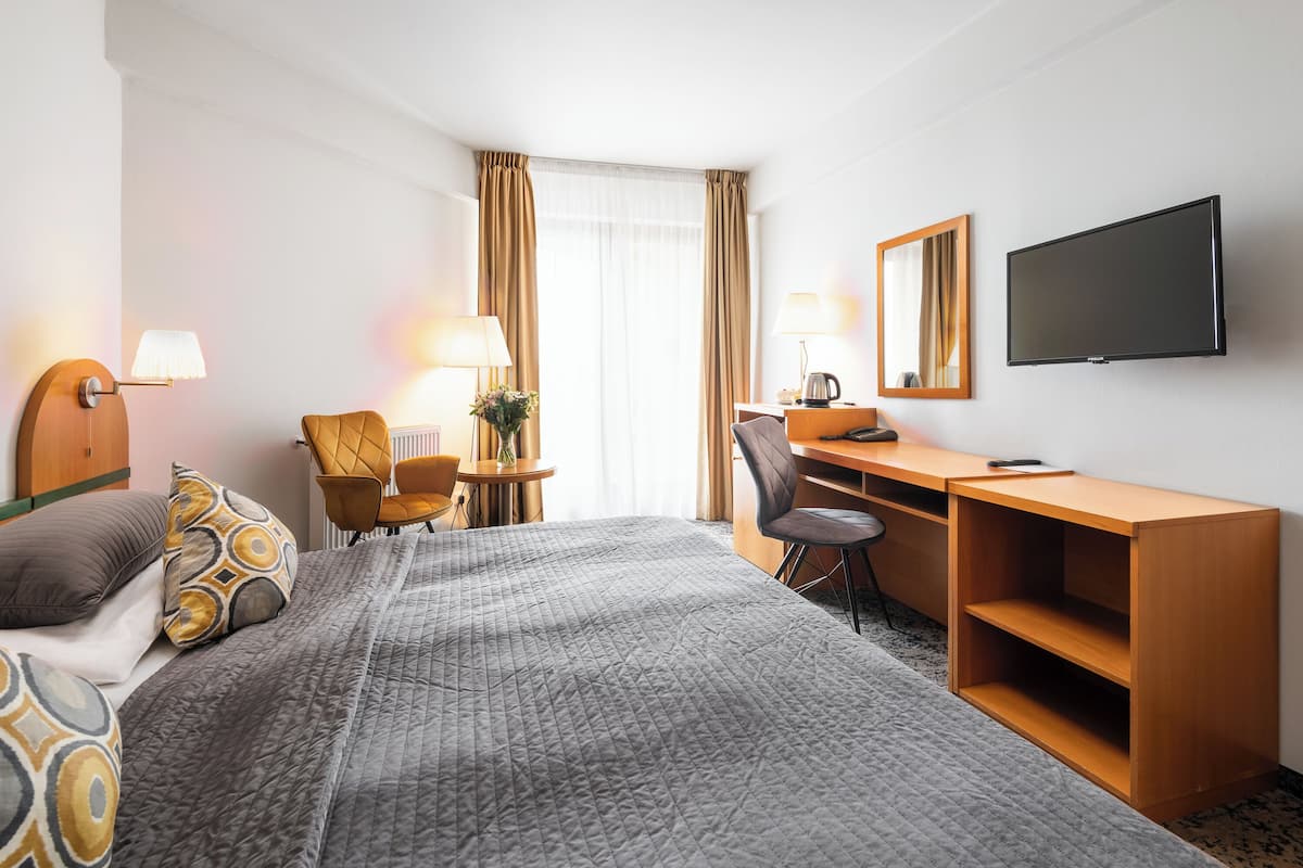 A hotel room with a bed, a desk, a chair, a television, and a window with curtains.