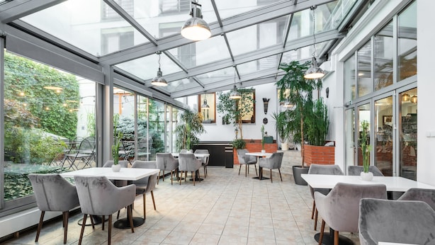 A modern indoor dining area with glass walls, grey upholstered chairs, and a tiled floor. - Hotel Troja (Prague)