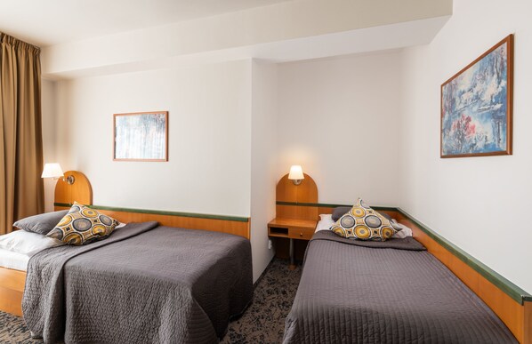 A hotel room with two single beds, each with a wooden headboard, a bedside table, and a lamp. There is a painting on the wall and a window with curtains. - Hotel Troja (Prague)