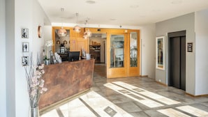 A hotel reception area with a wooden reception desk, pendant lighting, a glass door leading to a room, and a wall-mounted sign. - Hotel Troja (Prague)