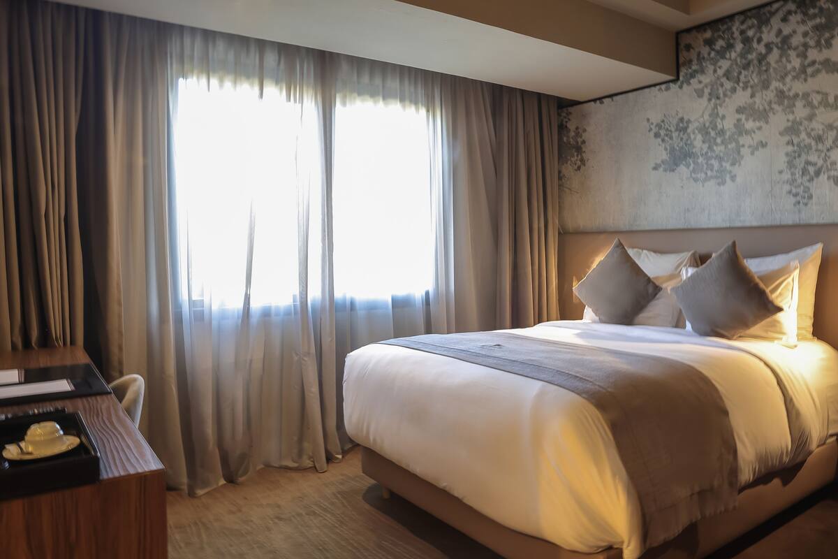 Una habitación de hotel con una cama grande, cortinas, un escritorio con silla y una pared con estampado floral.