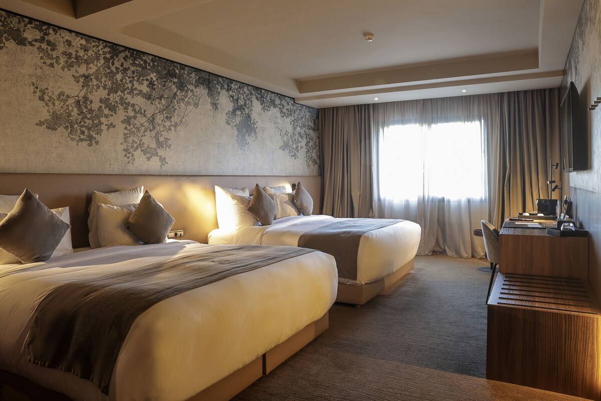 Habitación de hotel con dos camas grandes, un escritorio y un ventanal con cortinas.