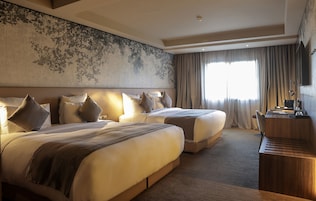 Habitación de hotel con dos camas grandes, un escritorio y un ventanal con cortinas.