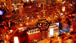 A bustling bar area with a large, circular wooden structure, multiple tables with patrons, and a well-stocked bar counter.