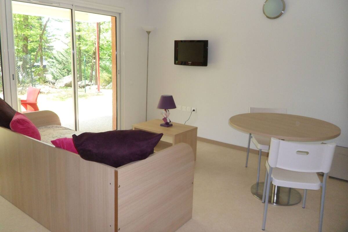 Una habitación moderna con sofá, una mesita, una silla y televisor en la pared.