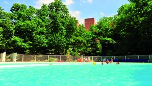 A swimming pool surrounded by lush green trees and a fenced area.